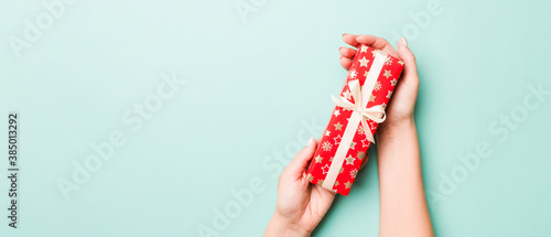 Woman hands give wrapped christmas or other holiday handmade present in colored paper. Present box, decoration of gift on Blue table, top view with copy space