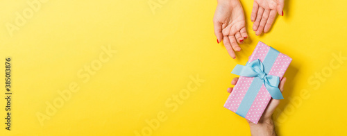 Top view of couple giving and receiving a gift on colorful background. Close up of romantic concept