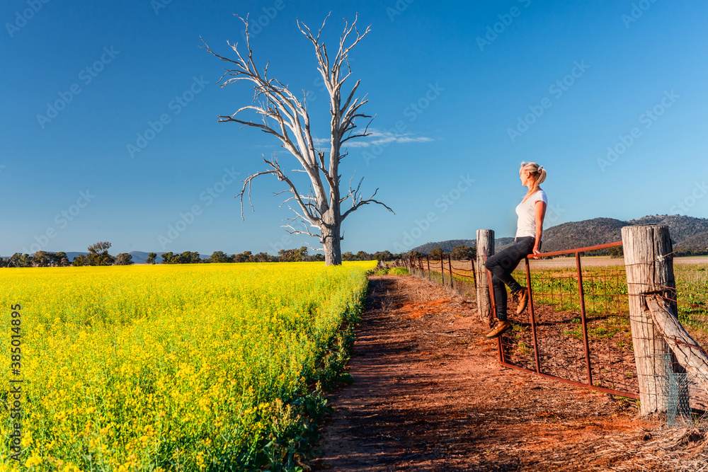 Country woman basking in the spring sunshine looking out over the fields of canola Country woman basking in the spring sunshine looking out over the fields of canola