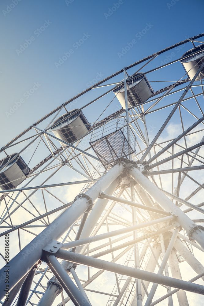Gray or white metal ferris wheel with closed passenger cabins close-up in the amusement park