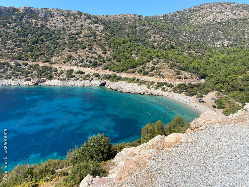 Beautiful turquoise sea bay coast on Aegean Sea. Variations of blue, green and turquoise colors of water. Green trees on the hills at the background.