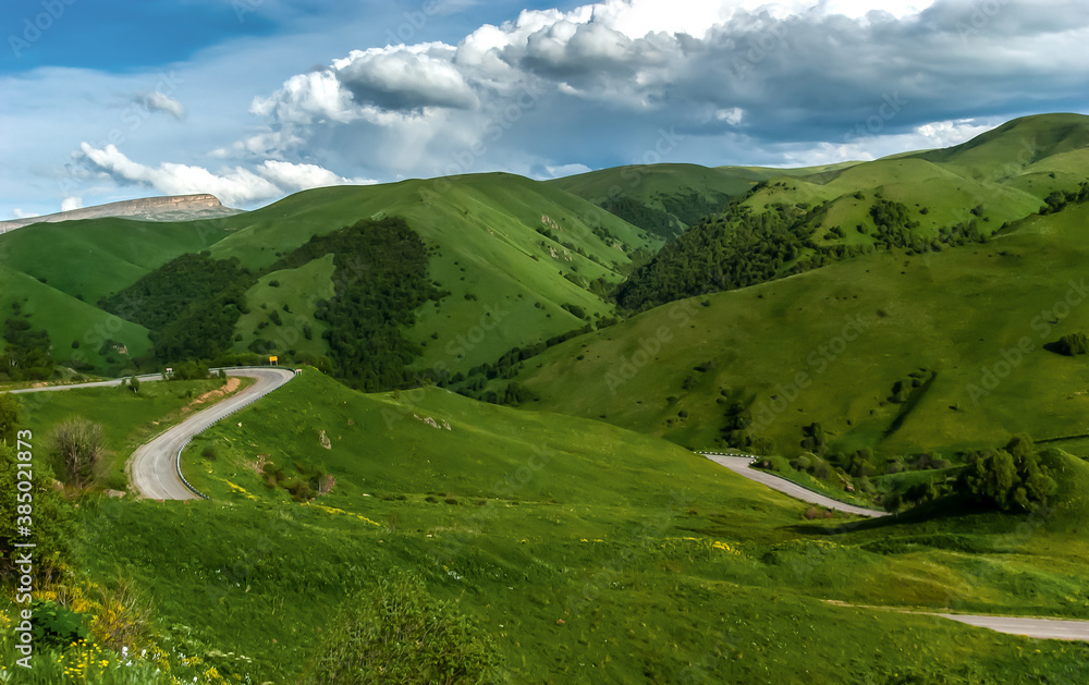 Endless green hills, a road appears and disappears among them. Hills of all kinds of shades of green, clouds. Foothills of the Caucasus Mountains. Russia.
