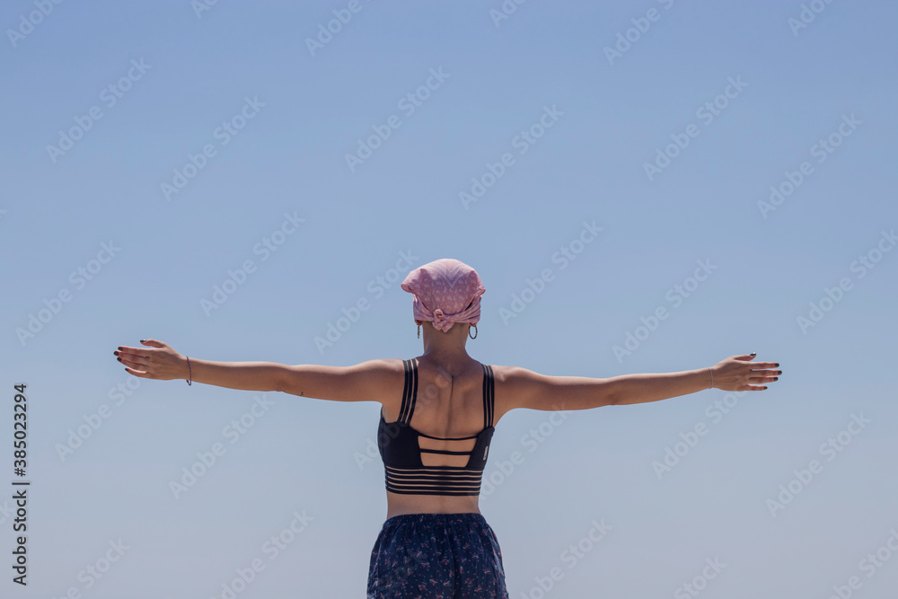 Mujer con pañuelo rosa de cancer de mama con los brazos abiertos de espalda - obrazy, fototapety, plakaty 