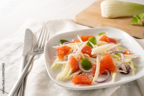 Fresh salad from raw fennel slices, grapefruit and red onions on a white plate, healthy vegetarian food, selected focus