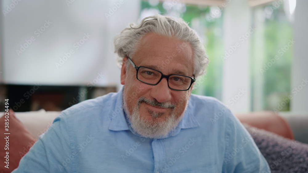 Senior man smiling at camera. Portrait of mature man sitting on couch in room Senior man smiling at camera. Portrait of mature man sitting on couch in room
