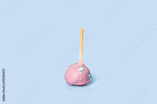 Chocolate dessert in pink glaze, round pastry on a wooden stick. Pink icing. Blue background.