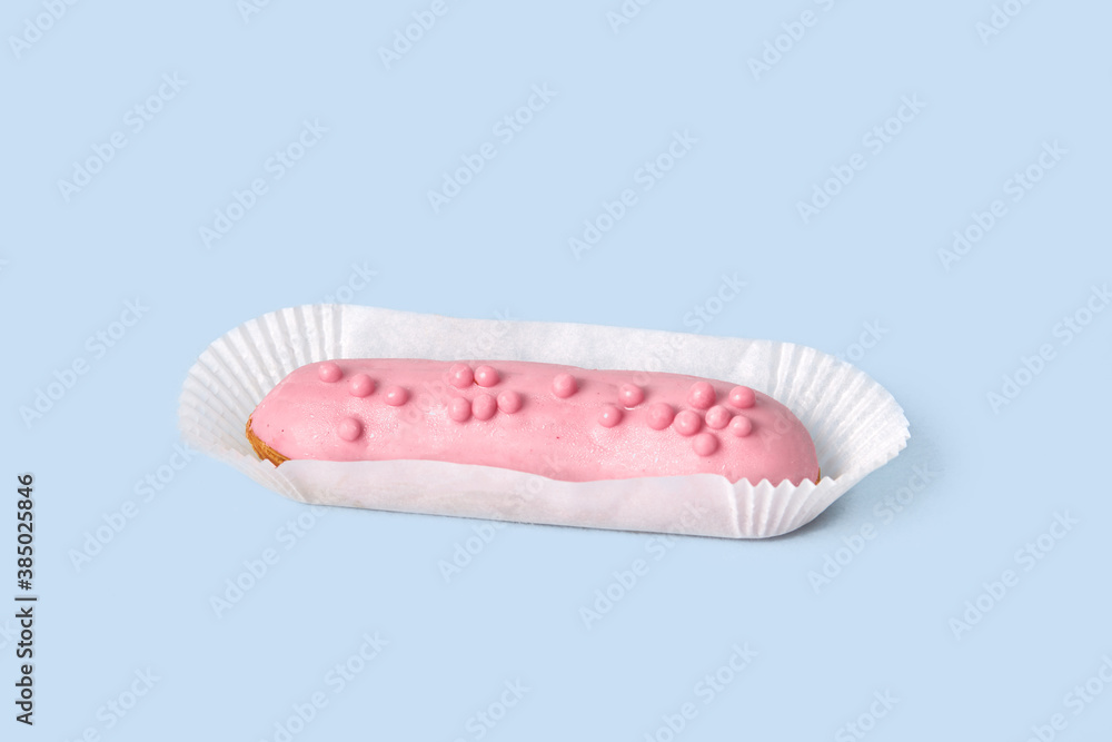 Beautiful bright Eclair in sweet pink glaze on white wrapping paper. Isolated on a blue background. Beautiful bright Eclair in sweet pink glaze on white wrapping paper. Isolated on a blue background.