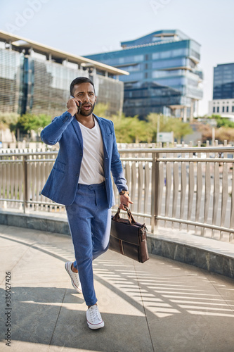Indian arabic businessman walking talking on mobile phone in city