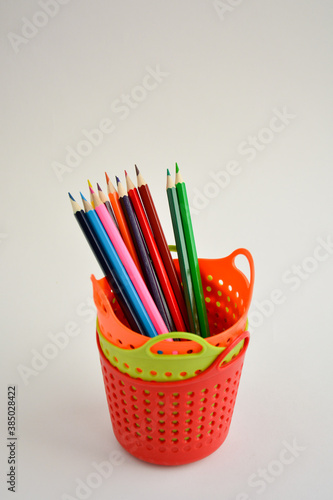 Colored sharpened pencils for drawing in a red pencil holder close-up on a light background