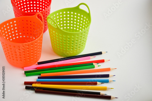 Colored sharpened pencils for drawing are next to multi-colored pencil holders close-up on a light background
