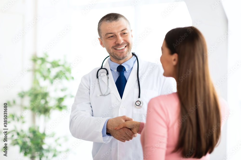 Portrait of middle aged doctor handshaking with his patient Portrait of middle aged doctor handshaking with his patient