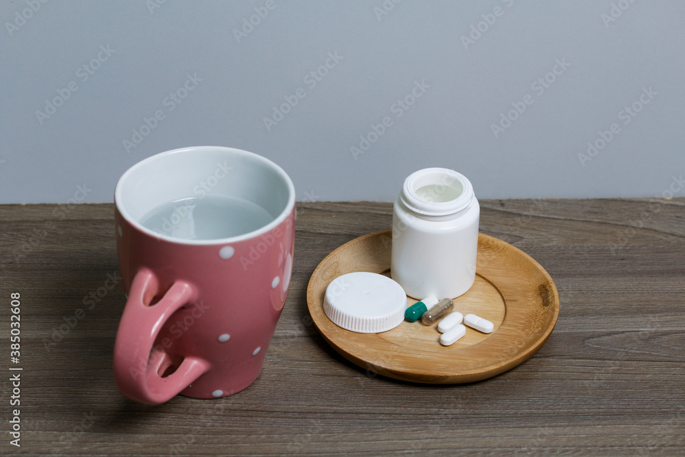 Container with pills and a mug of water. The lid of the container and several tablets are next to each other. Container with pills and a mug of water. The lid of the container and several tablets are next to each other.