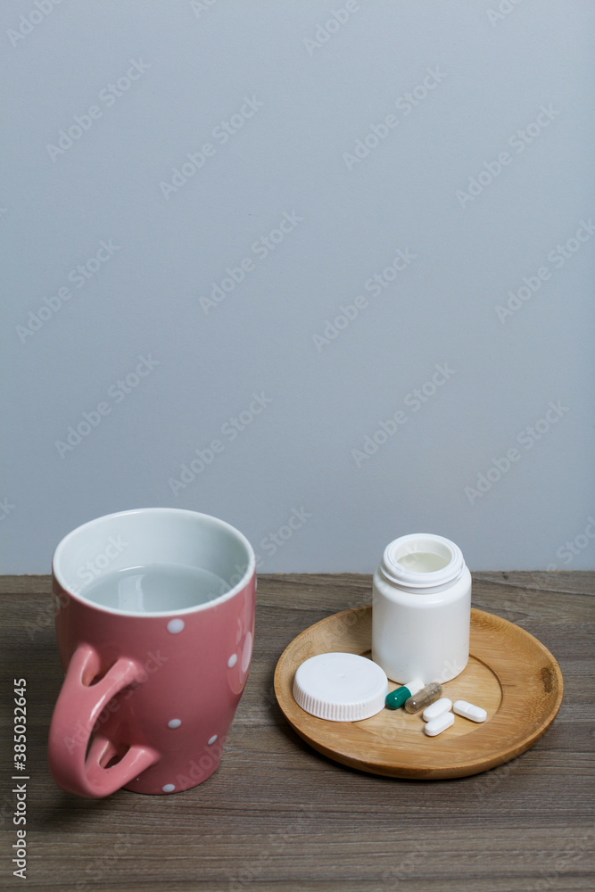 Container with pills and a mug of water. The lid of the container and several tablets are next to each other.