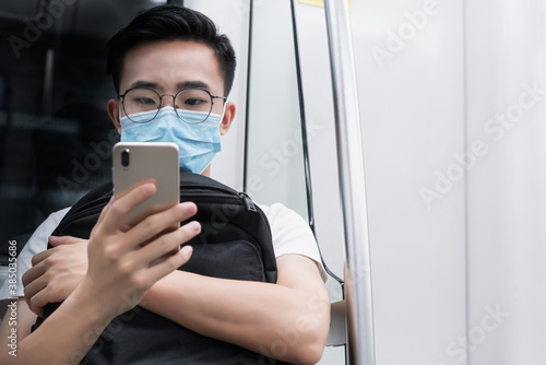 Young man wearing a mask sitting in the subway playing mobile phone