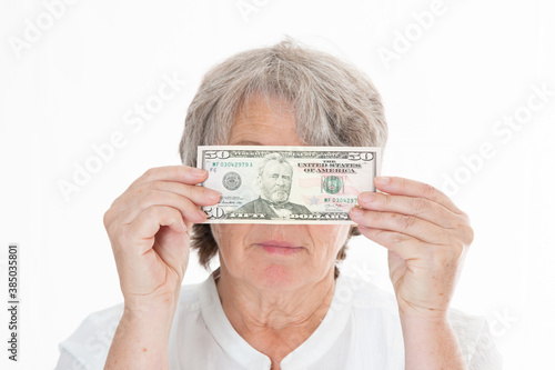 Seniorin hält sich Geld vor ihr Gesicht vor weißem Hintergrund