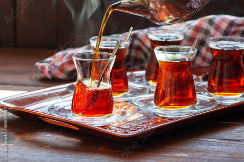 Glass cup of brewed black turkish tea pouring from teapot, traditional hot drink concept photo