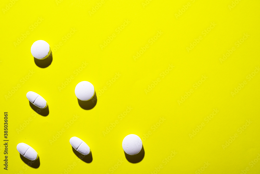 many white medical pills in a row on a yellow background. pills cast a shadow.