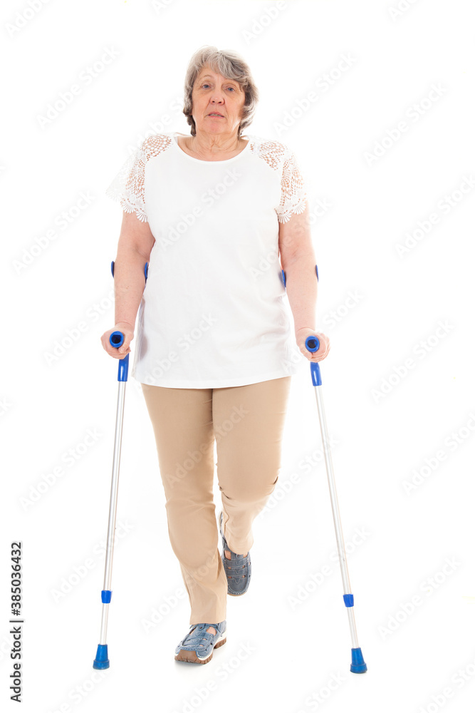 Seniorin steht auf Gehhilfen vor weißem Hintergrund Seniorin steht auf Gehhilfen vor weißem Hintergrund