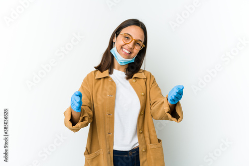 Young latin woman wearing a mask to protect from covid isolated on white background feels confident giving a hug to the camera.