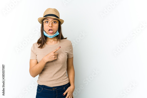 Young latin woman wearing hat and mask to protect from covid isolated on white background pointing to the side