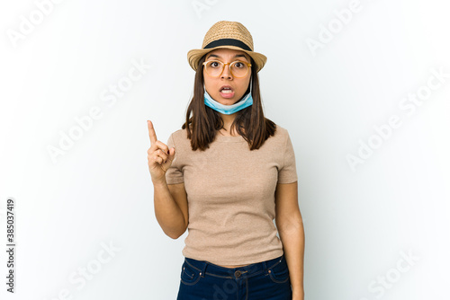 Young latin woman wearing hat and mask to protect from covid isolated on white background having an idea, inspiration concept.