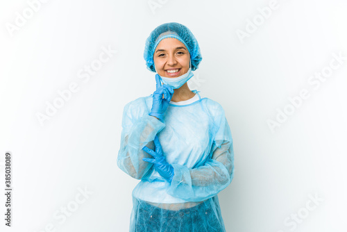 Young surgeon latin woman isolated on white background smiling happy and confident, touching chin with hand. © Asier