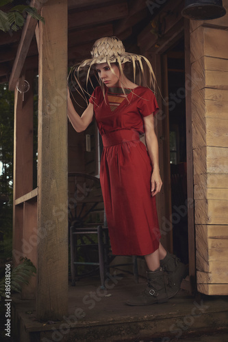 Young beautiful woman in a red casual dress, standing on the balcony of an old shack