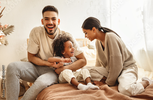 happy multi ethnic family mom, dad and child laughing, playing and tickles in bed at home.