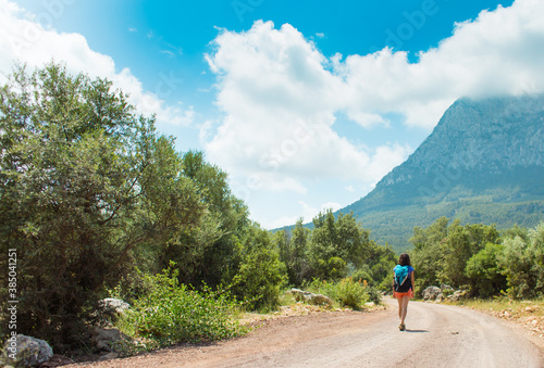 A woman with a backpack is walking along a mountain road.