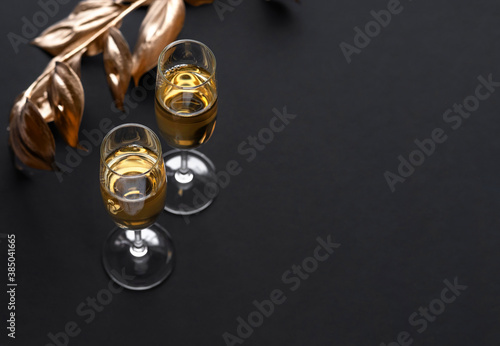 Two glasses of champagne over black background and golden Christmas decoration. Holiday decorations on dark table.