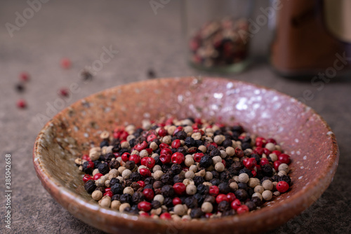 The beautiful spice blend is comprised of black, red, green, and white peppercorns in a small bowl on rustic table