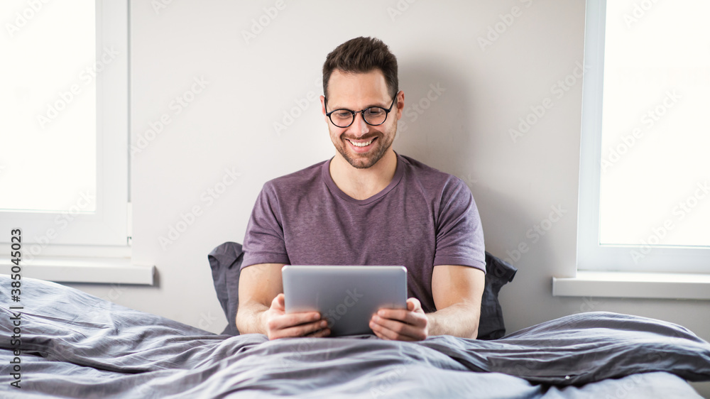 Man Using Digital Tablet Watching Movie Online Sitting In Bedroom Man Using Digital Tablet Watching Movie Online Sitting In Bedroom