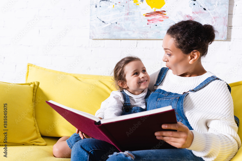 Mother holding book and embracing daughter at home Mother holding book and embracing daughter at home