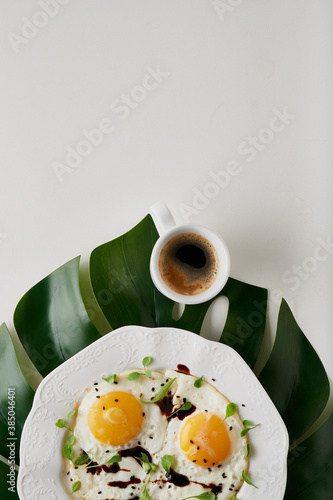 Morning breakfast with fried eggs and coffee in white cup and plant leaf on white table photo