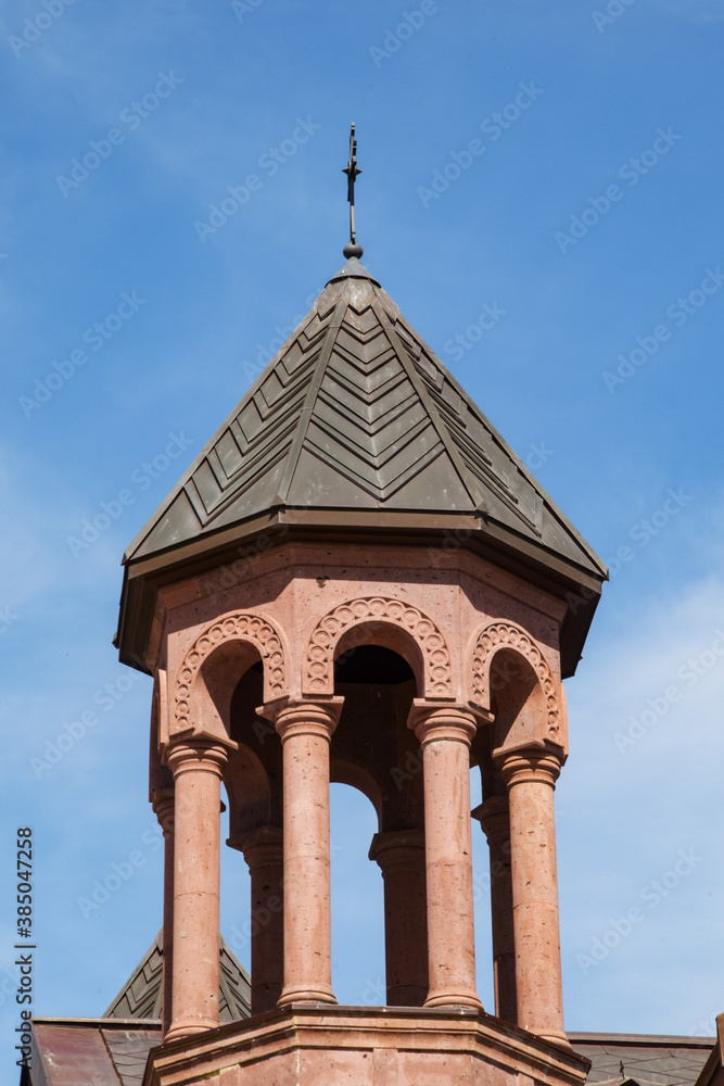 Bell tower of the Catholic Church in pink tuff. The cylindrical bell tower of the church against the background of a bright blue cloudless sky.