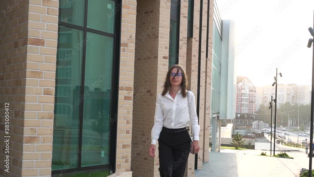 Business woman walks past a modern business center. Girl in a business suit looks at the clock and hurries. Business woman walks past a modern business center. Girl in a business suit looks at the clock and hurries.