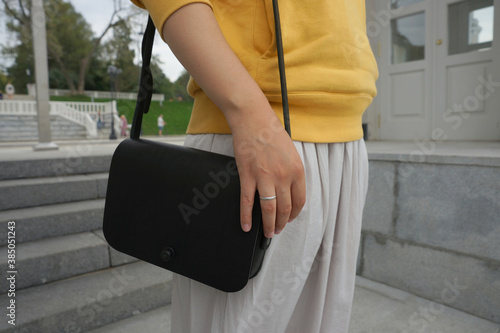 Woman with a yellow sweatshirt and white skirt with a black bag over her shoulder