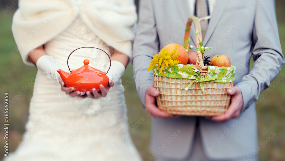 Vegetarian wedding. Autumn wedding details close up. Fiance with the bride at a picnic. Fruit basket and orange kettle. Wedding blog concept.