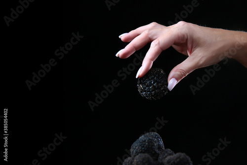 Black truffle in the woman's hand. Exquisite and fragrant mushroom. Unrecognizable person. Dark background. Close up.