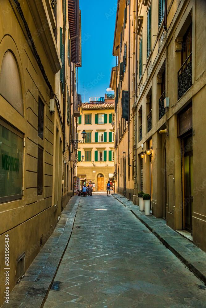 Nice portrait shot of the empty narrow alley Via dei Biffi in the old city centre of Florence, Tuscany, Italy on a sunny day with a blue sky.
