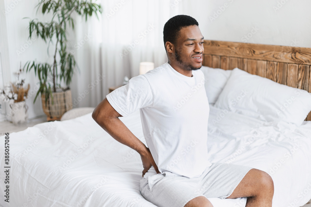 African American Man Touching Aching Back Sitting In Bed Indoors African American Man Touching Aching Back Sitting In Bed Indoors