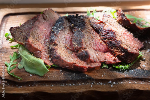 Medium rare baked veal with coarse salt, spices and arugula leaves on wooden background