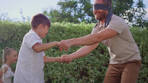 Parents with children playing blind man buff. Man eyes tied with blindfold