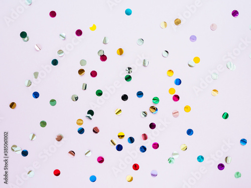 Multi-colored shiny round confetti on a pink background, top view, copy space, flat lay