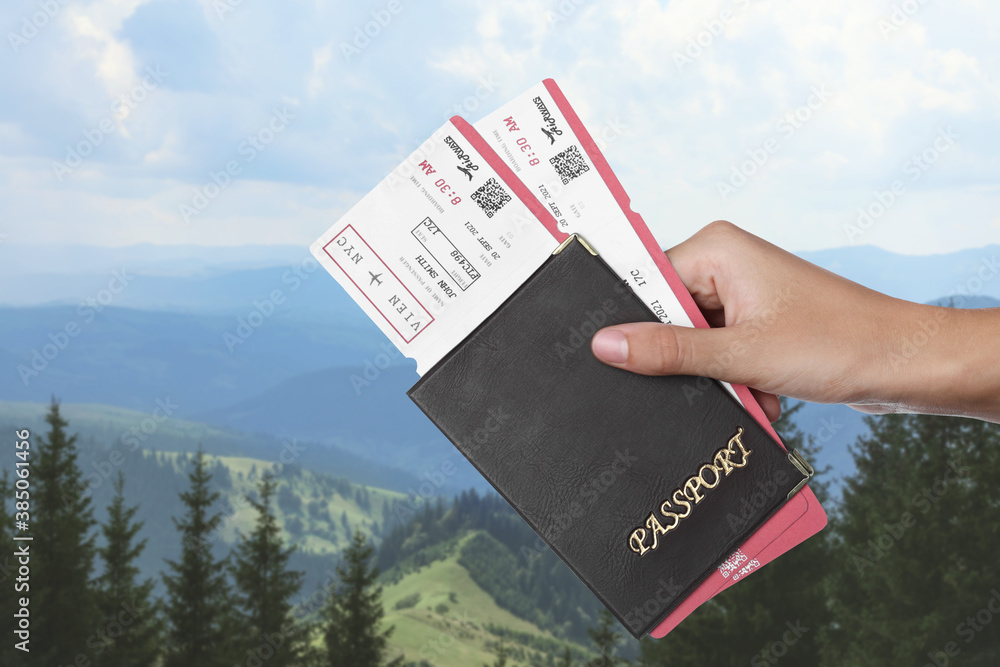 Woman holding passport with tickets in mountains, closeup. Travel agency service - obrazy, fototapety, plakaty 