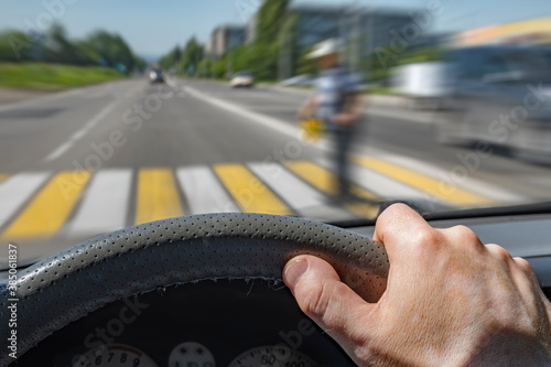 the driver hand on the steering wheel of a car moving at high speed and passing a pedestrian crossing with the risk of hitting a person photo