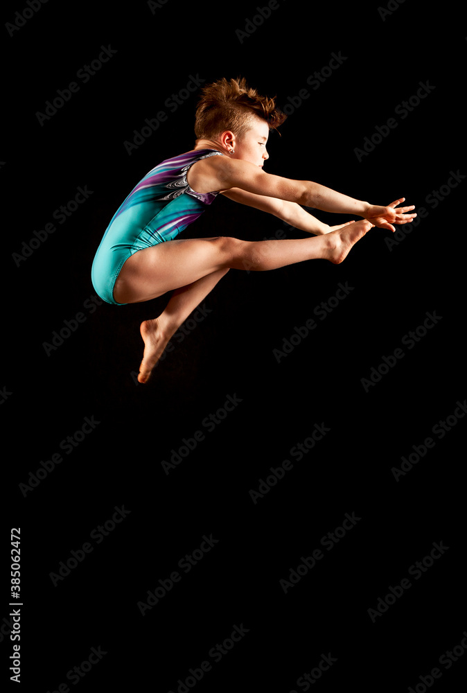 Youth gymnast executing a wolf jump on a black background. 