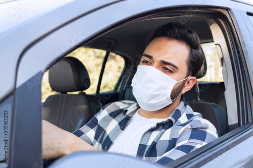 Portrait of young bearded man in a car. Lifestyle concept with handsome guy in a car who using medical face mask