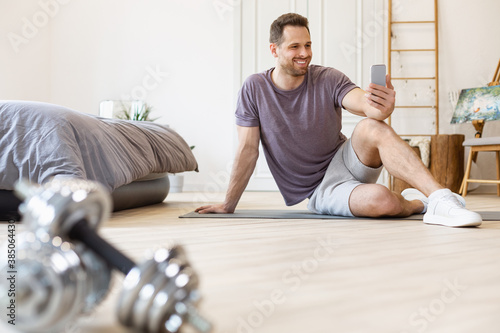 Man Training Using Smartphone Exercising Sitting On Mat At Home