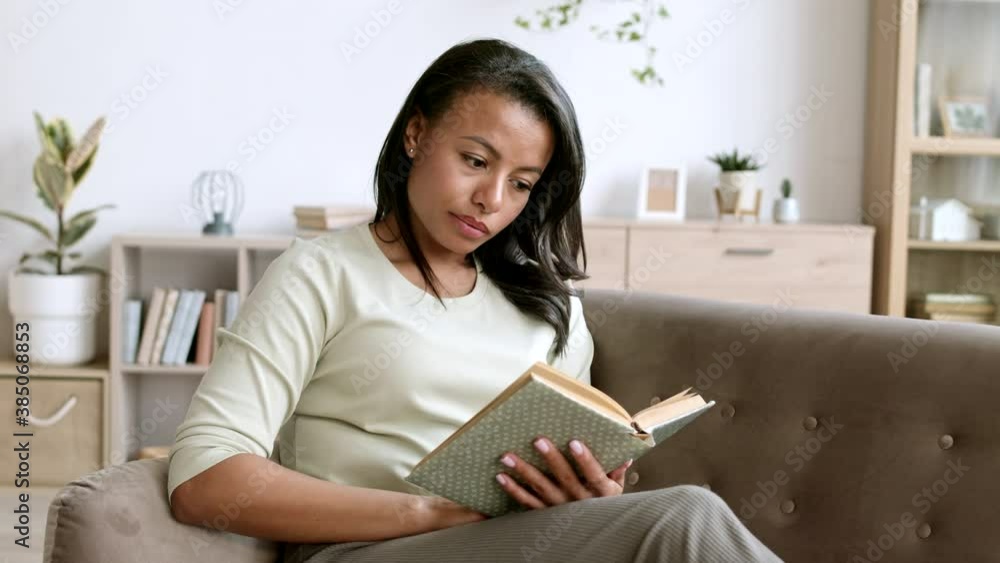 Medium shot of attractive mixed-race woman wearing casual clothes sitting on couch at home and reading book Medium shot of attractive mixed-race woman wearing casual clothes sitting on couch at home and reading book